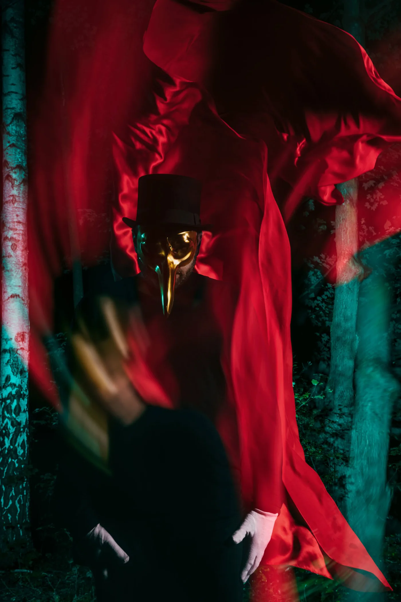 Claptone in a swirling red cloak among dark trees, white gloves raised